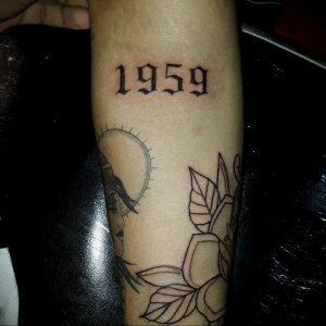 Фото тату: татуировка с годом '1959' в готическом стиле на мужском предплечье. Черный цвет, острые углы, выразительный дизайн.
