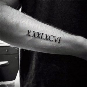 Фото тату: черная татуировка с римскими цифрами 'X.XXXI.XCVII' на мужском предплечье. Классический стиль, четкие линии, минималистичный дизайн.