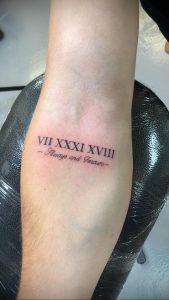 Фото тату: римские цифры 'VII XXXI XVIII' и надпись 'Always and Forever' на предплечье, выполненные черным шрифтом. Романтичная татуировка.