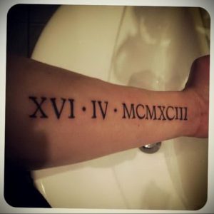 Фото тату: черные римские цифры 'XVI.IV.MCMXCIII' на внутренней стороне руки, выполненные четким шрифтом. Простой и элегантный рисунок татуировки.