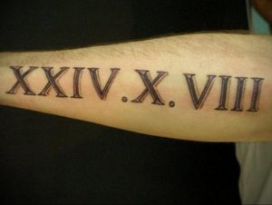 Фото тату: черные римские цифры 'XXIV.X.VIII' на предплечье, выполненные четкими линиями. Минималистичный рисунок татуировки для мужчин и женщин.