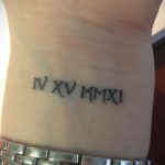 Фото татуировки с римскими цифрами IV XV MM XXI на запястье. Минималистичный дизайн, выполненный черными чернилами.