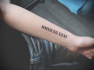 Фото татуировки с римскими цифрами MMXXII XII XXXI на запястье. Минималистичный дизайн, выполненный черными чернилами.