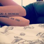 Фото тату: на бедре выгравированы римские цифры 'XXXI X MCLXIV' и 'IIX MCM III XX' черными чернилами. Минималистичный стиль, длинная татуировка.
