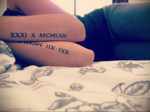 Фото тату: на бедре выгравированы римские цифры 'XXXI X MCLXIV' и 'IIX MCM III XX' черными чернилами. Минималистичный стиль, длинная татуировка.