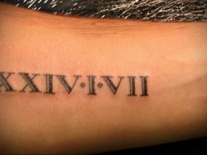 Фото тату: черные римские цифры XXIV.I.VII на руке, выполненные четкими линиями, минималистичный дизайн.