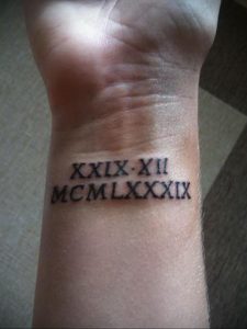 Фото тату: римские цифры XXIX-XII MCM LXXXIX на запястье, выполненные черными чернилами, с четкими линиями.