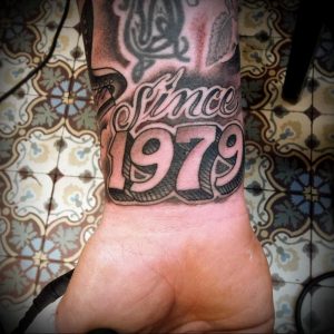 Фото тату: татуировка 'Since 1979' с изображением символа и орнамента на запястье. Классический стиль, четкие линии, мужской дизайн.