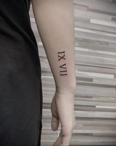Фото тату на предплечье: черные римские цифры IX VII, выполненные в минималистичном стиле. Простой и элегантный рисунок татуировки.