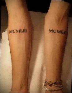 Фото парных татуировок с римскими цифрами 'MCMLIII' и 'MCMLV' на предплечьях. Черный цвет, минималистичный дизайн, символизирующий важные даты.