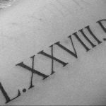 Фото татуировки с римскими цифрами 'L.XXVIII.R' на руке. Черный цвет, классический стиль, минималистичный дизайн, символизирующий дату или инициалы.