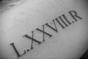 Фото татуировки с римскими цифрами 'L.XXVIII.R' на руке. Черный цвет, классический стиль, минималистичный дизайн, символизирующий дату или инициалы.