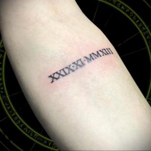 Фото татуировки с римскими цифрами 'XXXIX-MMXIII' на предплечье. Черный цвет, четкие линии, минималистичный дизайн, символизирующий важную дату.