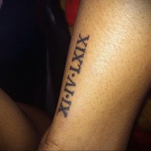 Фото тату с римскими цифрами 'XI-IV-LXIX' на руке. Стиль татуировки - минимализм, тонкие черные линии.