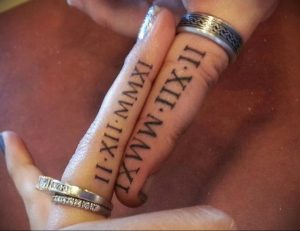 Фото парных тату с римскими цифрами 'II-XII-MMXI IX-WMMXI' на пальцах. Стиль татуировки - минимализм, тонкие черные линии.