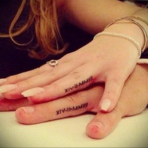 Фото парных тату с римскими цифрами 'XIV-II-MMXXII' на пальцах. Стиль татуировки - минимализм, тонкие черные линии.