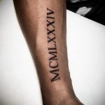 Фото тату с римскими цифрами 'MCMXLXXIV' на руке. Стиль татуировки - минимализм, четкие черные линии.