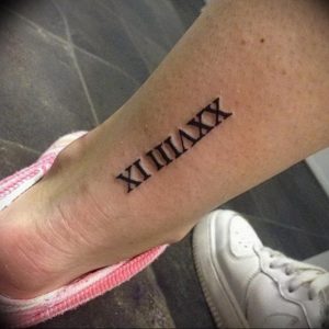 Фото татуировки с римскими цифрами XI III VIII XX на лодыжке. Черно-белый рисунок, выполненный тонкими линиями, выглядит изящно и женственно.