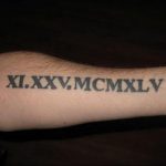 Фото татуировки с римскими цифрами XI.XXV.MCMXLV на предплечье. Черно-белый рисунок, выполненный четким шрифтом, выглядит строго и лаконично.