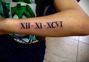 Фото тату: На запястье изображены римские цифры 'XII-XI-XCVI' черным цветом, создавая лаконичный и стильный рисунок.