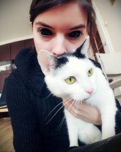 Фотография девушки, держащей черного с белым котенка. Улыбка, уютная атмосфера, теплые тона.