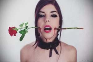 Фотография девушки с красной розой в губах, символизирующая страсть и боль. Драматичный макияж, капли крови.