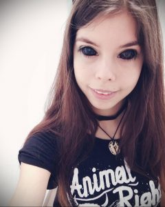 Портрет девушки с длинными темными волосами и футболкой с надписью "Animal Riot". Выразительный взгляд и легкий макияж.
