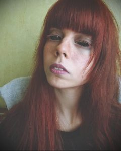 Фотография девушки с рыжими волосами, смотрящей в камеру с задумчивым выражением лица. На девушке легкий макияж.