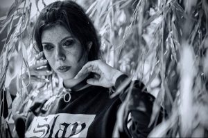 Черно-белый портрет молодой девушки с веснушками. Она смотрит в камеру с задумчивым выражением лица. Ее волосы слегка растрепаны, а на шее чокер.