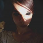 Фотография молодой женщины, лицо которой частично освещено лучом света. Образ создает атмосферу таинственности и загадочности.