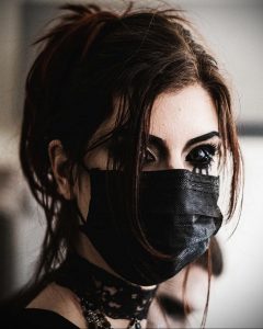 Фотография женщины в черной маске, закрывающей нижнюю часть лица. Образ создает атмосферу таинственности и опасности.