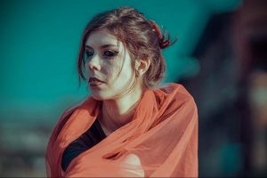 Фотография молодой женщины в оранжевом платке, смотрящей в сторону. Образ создает атмосферу восточной сказки и загадочности.