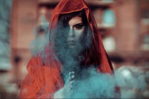 Фотография женщины в красном платке, лицо которой частично скрыто дымом. Образ создает атмосферу загадочности и мистики.