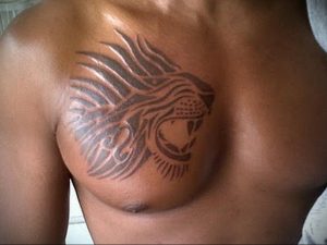 Фото татуировки льва на груди, выполненной в стиле трайбл с использованием черных линий и геометрических узоров. Подчеркивает мужественность и силу.