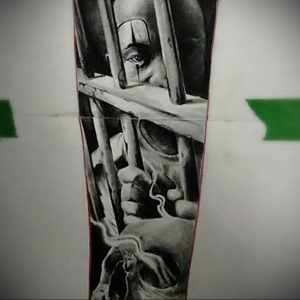 Фотография татуировки в стиле blackwork, изображающей лицо заключенного за решеткой и череп в нижней части рукава. Черно-белое изображение.