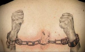 Черно-серая татуировка на спине с изображением разорванных цепей, удерживаемых сильными руками, символизирующая освобождение и силу духа.