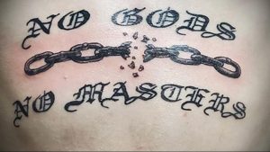 Фото тату на теле: надпись "No Gods No Masters" с изображением разорванных цепей. Символизирует анархию, свободу и независимость.