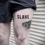 Фото татуировки на бедре с надписью "SLAVE" и изображением автомобильной фары, символизирующей зависимость и контроль. Черно-белый рисунок.