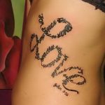 Фото тату: черная татуировка надписью "Love" в форме змеи, обвивающей бок женщины. Изящный рисунок татуировки с религиозным подтекстом.
