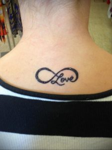 Фото тату с изображением символа бесконечности, внутри которого написано слово 'Love'. Татуировка выполнена в черном цвете и расположена на спине.