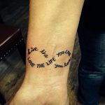 Фото тату на запястье с надписью 'Live the life you love'. Текст закручен в форме сердца, выполнен черными чернилами.