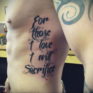 Фото татуировки с надписью 'For those I love I will Sacrifice' на боку мужчины. Черный цвет, каллиграфический шрифт.