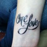 Фото татуировки с надписью 'One Love' на запястье. Черный цвет, каллиграфический шрифт, стильный дизайн.