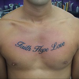 Фото татуировки с надписью 'Faith Hope Love' на груди мужчины. Темно-синий цвет, каллиграфический шрифт.