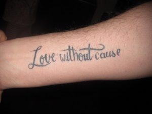 Фото тату на предплечье: надпись "Love without cause" черными чернилами, выполненная рукописным шрифтом. Философская и вдохновляющая татуировка.