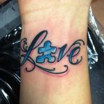 Фото тату на запястье: надпись "Love" в ярких розовых и голубых тонах с акварельным эффектом. Современный и стильный дизайн.