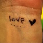 Фото простой татуировки на запястье с надписью 'love' и небольшим сердцем. Черно-серый рисунок, выполненный в наивном стиле.
