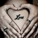 Фото татуировки на груди в форме сердца, внутри которого написано слово 'Love'. Черно-серый рисунок.