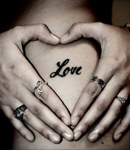 Фото татуировки на груди в форме сердца, внутри которого написано слово 'Love'. Черно-серый рисунок.