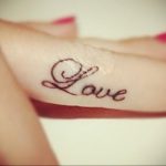 Фото татуировки надписи "Love" выполненной каллиграфическим шрифтом на пальце. Черно-белая татуировка, минималистичный дизайн, популярный выбор для девушек.
